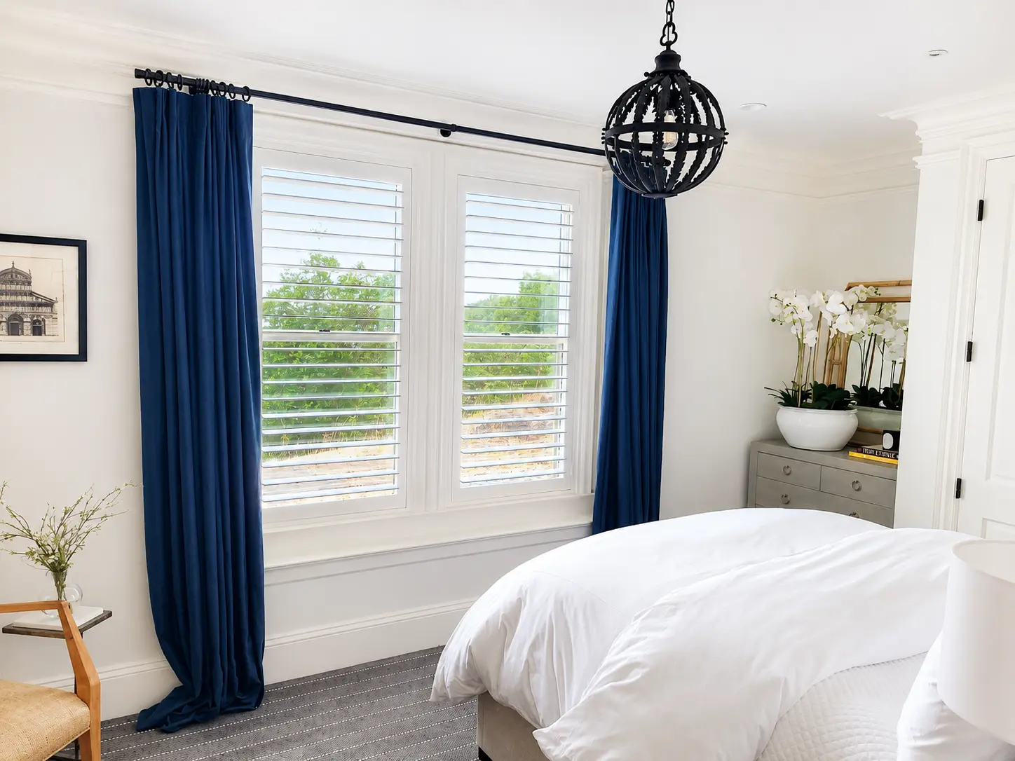 White plantation shutters paired with blue drapery in a bright bedroom
