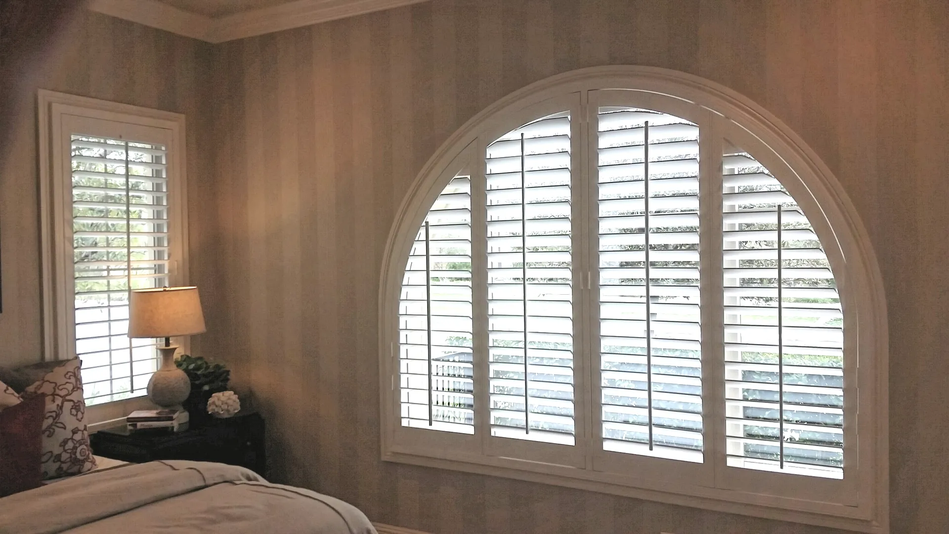White half-round arched plantation shutters with four operable panels on a wide bedroom window
