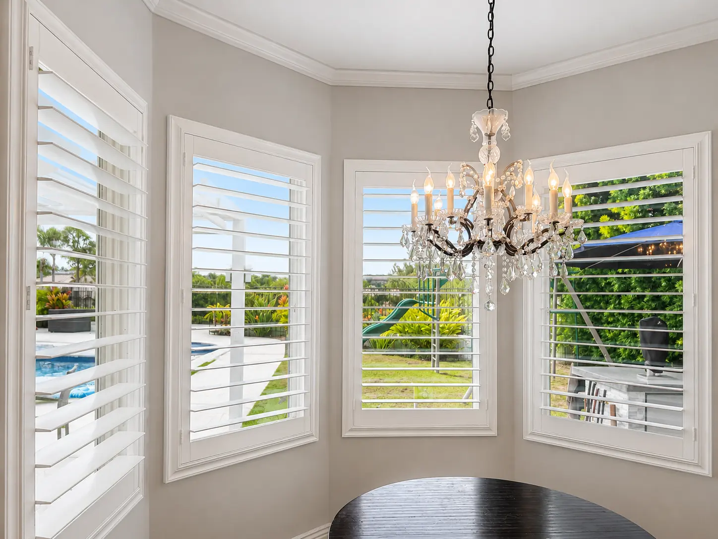 White wood plantation shutters wrapping a bay-window breakfast nook with a crystal chandelier