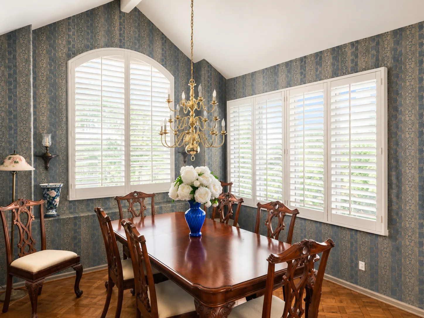 White arched-top plantation shutter and four-panel window shutters in a formal dining room with blue wallpaper