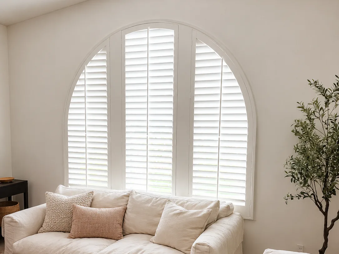 White arched-top plantation shutter above a cream sofa in a neutral living room