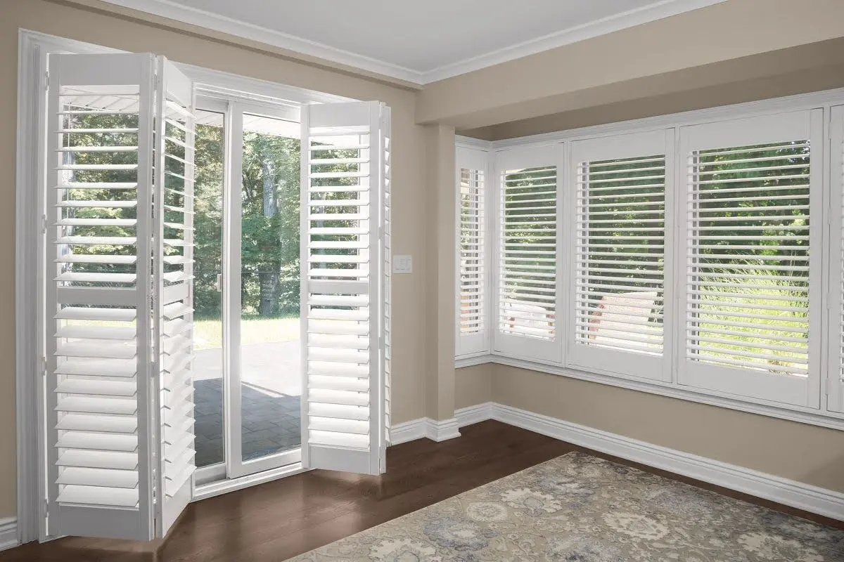 White bi-fold plantation shutters on a patio door beside a bay window