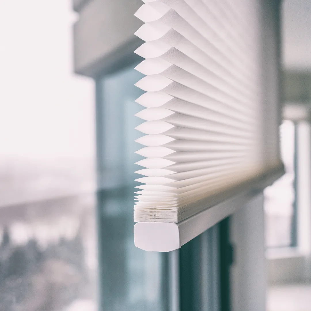 Close-up of a white honeycomb cellular shade raised beside a bright window