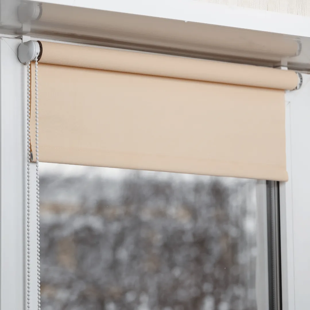 Beige roller shade partially lowered over a window on a cool winter day